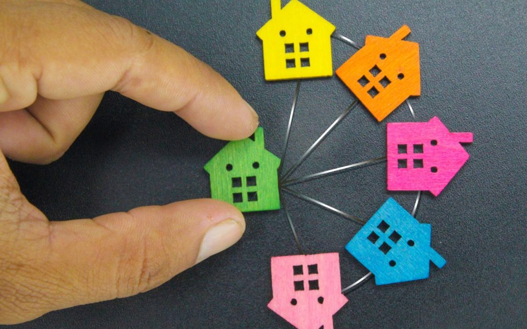 Self-managed HOA A hand placing a wooden cutout of a house on a table next to other house cutouts.