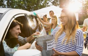 A woman in a car ads money to a donation bucket during a carwash fundraiser