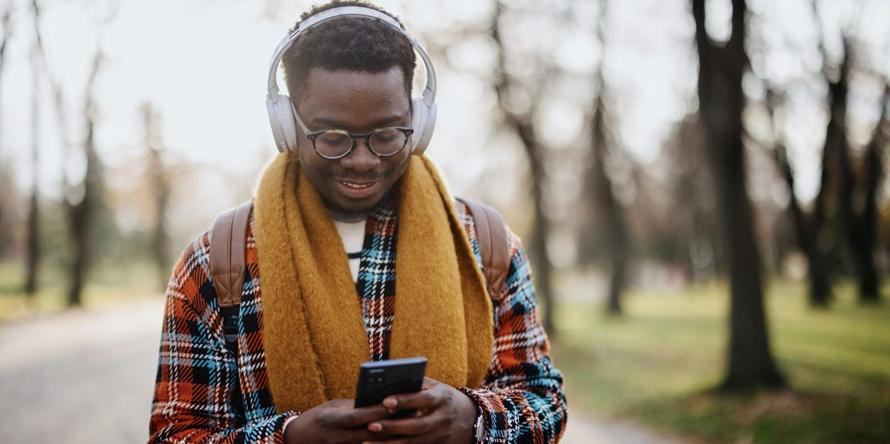 Young black man walking in the park while listening to the music on his wireless headphones